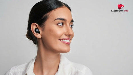 A woman wearing a black Sabertooth Pro wireless earbud, shown in profile against a light gray background with the Sabertooth Pro logo in the top right corner.